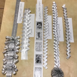 May include: A collection of six silver ribbon homecoming mum braids and chains labeled as Loop Chain, Texas, Custom Photo Chain, Diamond Back, Military Braid, and Mobius. The items feature various woven patterns, silver glitter accents, and photo frames.