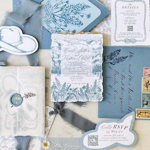 May include: A wedding stationery suite in shades of dusty blue and white, featuring a deckled-edge invitation, RSVP card with QR code, details card, envelopes, and blue silk ribbons. The set includes floral illustrations, a wax seal, and vintage stamps.