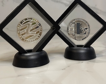 Può includere: Due monete d'argento Litecoin in teche nere con coperchi trasparenti. Le monete presentano il logo Litecoin e il testo "Vires in Numeris - 2013 25 Litecoins".