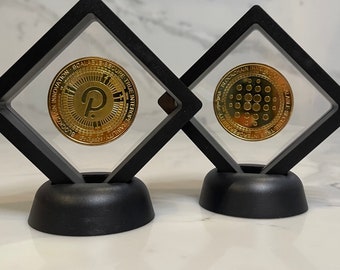 Può includere: Due monete di criptovaluta dorate esposte in teche quadrate nere con frontali in plastica trasparente. La moneta a sinistra ha una "P" al centro e il testo "BLOCKCHAIN INNOVATION SCALE SECURE TRUE INTEGRATED" attorno al bordo. La moneta a destra ha un cerchio di punti al centro e il testo "WEB3.0 BLOCKCHAIN INNOVATION SCALE SECURE TRUE INTEGRATED" attorno al bordo.
