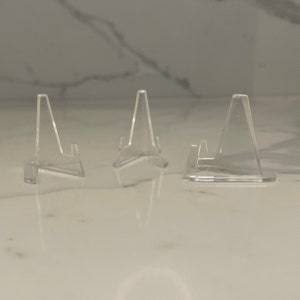 以下が含まれることがあります： 3つの透明なアクリル製ディスプレイスタンド。サイズはそれぞれ異なります。スタンドは三角形で、上部に小さなリップがあり、オブジェクトを保持できます。