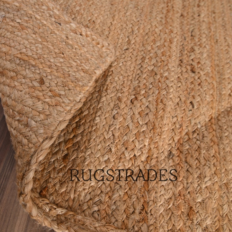 May include: Close-up of a natural fiber rug made from woven jute. The rug has a light brown color and a textured surface. The text "RUGSTRADES" is visible in the lower center of the image.