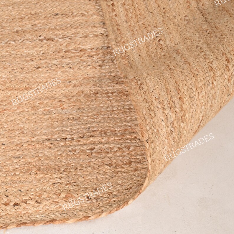 Pu&ograve; includere: Primo piano di un tappeto in fibra naturale realizzato in juta. Il tappeto ha una trama tessuta e un colore marrone chiaro. Il tappeto &egrave; piegato a met&agrave;, mostrando il bordo del tappeto.