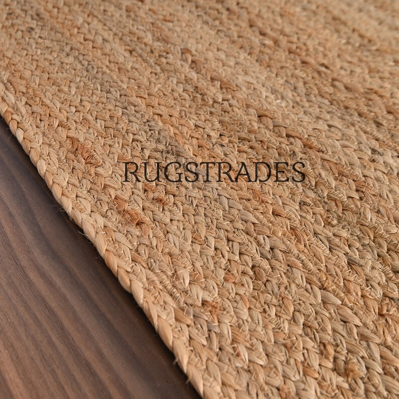 May include: A close-up of a natural fiber rug made from jute. The rug has a woven texture and a light brown color. The text "RUGSTRADES" is visible in the image.