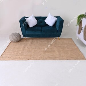 Pu&ograve; includere: Un tappeto in juta marrone chiaro con un divano in velluto turchese con due cuscini bianchi e un pouf rotondo grigio di fronte.