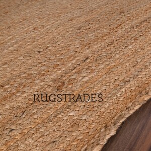 May include: A close-up of a natural fiber rug made from jute. The rug has a woven texture and a light brown color. The rug is made of natural materials and is perfect for adding a touch of rustic charm to any room.