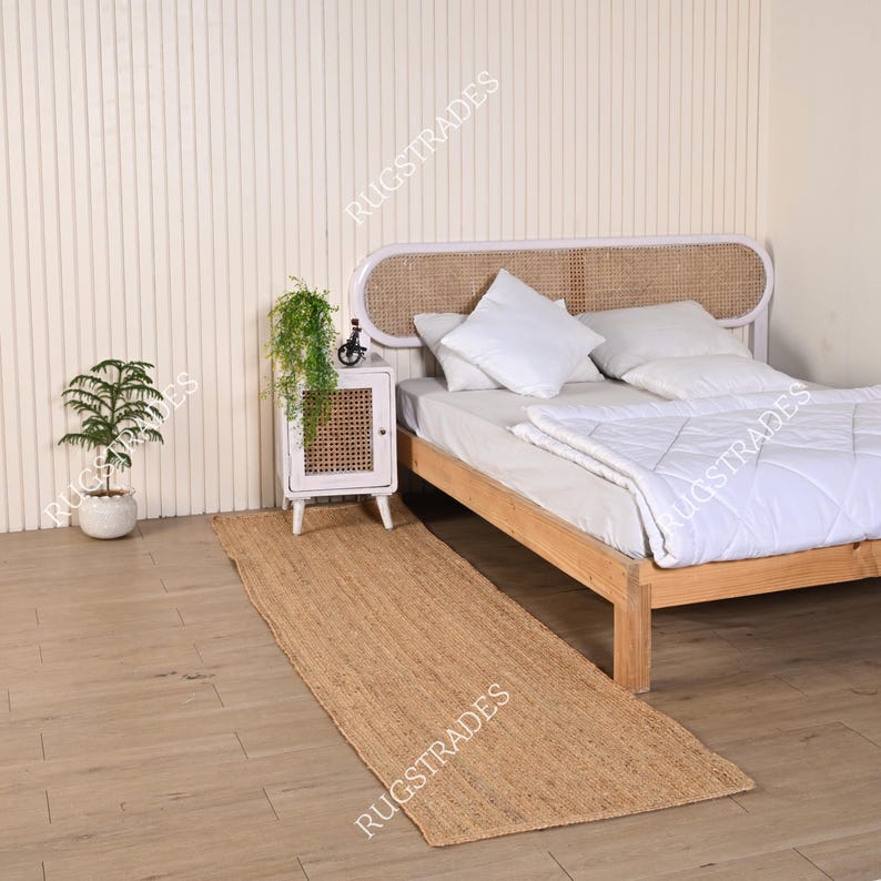 Pu&ograve; includere: Un runner per tappeto in juta naturale di colore marrone chiaro. Il tappeto &egrave; posizionato davanti a un letto bianco con una testata intrecciata e biancheria da letto bianca. Un comodino bianco con una porta intrecciata si trova accanto al letto.
