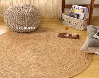 Può includere: Un tappeto rotondo in iuta naturale con un motivo a spirale. Un pouf beige lavorato a maglia e un cestino intrecciato con libri sullo sfondo. Il tappeto misura circa 152 cm di diametro, perfetto per un soggiorno o una camera da letto.