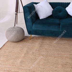 Pu&ograve; includere: Un tappeto in juta marrone chiaro con un divano in velluto turchese e un pouf in maglia grigia sullo sfondo.