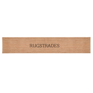 Puede incluir: Una alfombra rectangular tipo pasillo hecha de fibras tejidas de color canela natural con una superficie texturizada. La palabra RUGSTRADES est&aacute; impresa en letras may&uacute;sculas negras en el centro de la alfombra, con un tejido denso y marr&oacute;n.