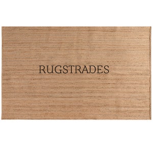 May include: A natural fiber rug with a woven texture in a light brown color. The rug has the text "RUGSTRADES" printed in black.