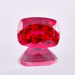 May include: A vibrant red gemstone with a cushion cut. The gemstone is faceted and has a high level of brilliance.