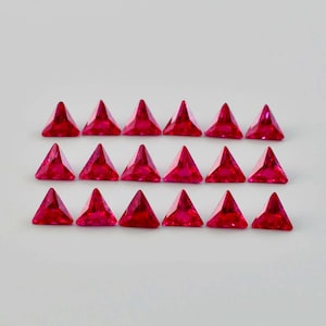 Könnte beinhalten: Vierundzwanzig dreieckige Rubingesteine, angeordnet in zwei Reihen zu zwölf. Die Edelsteine sind in einem leuchtenden Rot und haben einen facettierten Schliff.