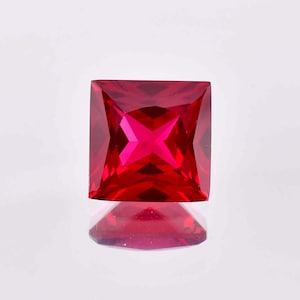 Könnte beinhalten: Ein leuchtend roter quadratischer Edelstein mit facettiertem Schliff. Der Edelstein reflektiert das Licht und erzeugt einen funkelnden Effekt.