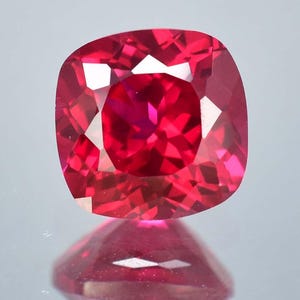 May include: A vibrant red gemstone with a cushion cut. The gemstone is faceted and has a high polish.
