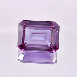 May include: A purple emerald cut gemstone with a slight pink hue.
