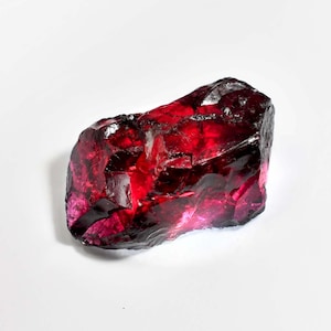 May include: A large, deep red, faceted gemstone with a rough, natural shape.