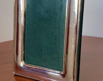 May include: A silver picture frame with a green velvet backing. The frame has a rounded top and a smooth, polished finish.