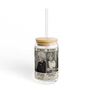 Puede incluir: Un vaso de vidrio transparente con tapa de bambú y una pajita. El vaso tiene una imagen en blanco y negro de tres mujeres con el texto "BE BRAVE BE HUMBLE" y las citas "When you are scared" y "When you are victorious".