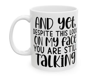 May include: White ceramic coffee mug with black text that reads "And yet, despite this look on my face you are still talking".