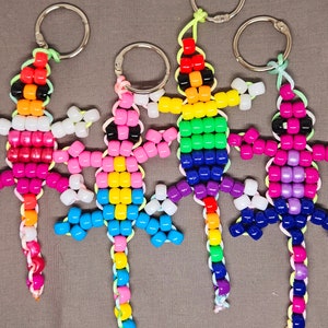 May include: Five colorful beaded keychains shaped like lizards. Each keychain is made with small, colorful beads and has a silver key ring attached.