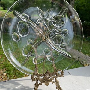 May include: A clear glass serving dish with a starburst design and four divided sections. The dish is on a gold metal stand.