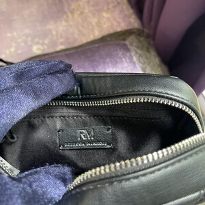 May include: Black leather crossbody bag with a silver zipper and studded accents. The interior features a black lining and a label that reads "RM REBECCA MINKOFF". The bag is open, revealing the inside.