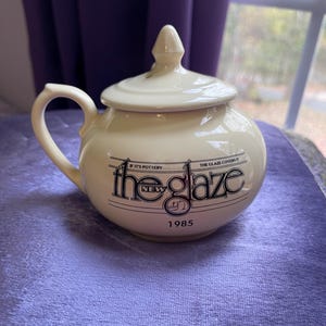 May include: A white ceramic sugar bowl with a black and white logo that reads "The Glaze" with the words "If it's pottery, the glaze covers it" and "New" above the logo and "1985" below the logo.