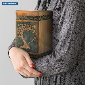 May include: Wooden urn with a tree of life design carved into a green panel. The urn is rectangular with a decorative border and the text "THE KNOX CRAFT" in the upper left corner.