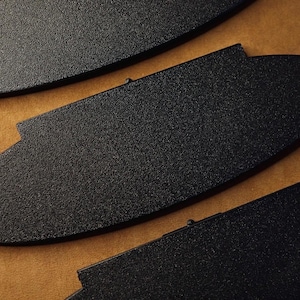 May include: Close-up of three black, textured, oval-shaped objects with a small rectangular notch on one side. The objects are arranged on a brown surface, with the focus on their shape and texture.