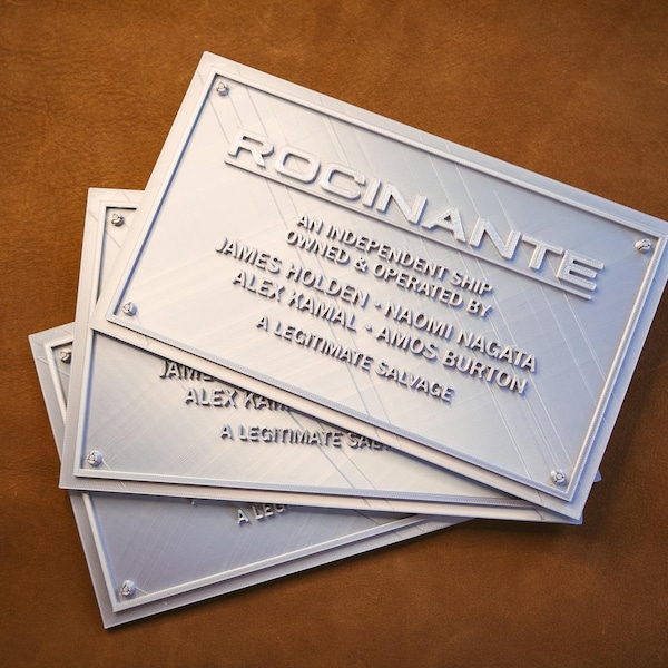 May include: Three silver rectangular plaques with the word "ROCINANTE" embossed at the top. The plaques have text that reads "AN INDEPENDENT SHIP OWNED & OPERATED BY JAMES HOLDEN - NAOMI NAGATA ALEX KAMAL - AMOS BURTON A LEGITIMATE SALVAGE."