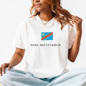May include: A white short-sleeved t-shirt featuring a centered graphic of the flag of the Democratic Republic of the Congo above the black text "baza maîtrisable". The shirt has a crew neckline and a standard fit, providing a clean look.