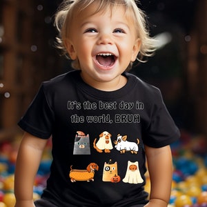 Può includere: Una maglietta nera con la scritta "It's the best day in the world, BRUH" e animali dei cartoni animati a tema Halloween. La maglietta è indossata da un bambino sorridente.