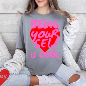 May include: A grey t-shirt with a pink and red heart graphic that says "Being Your Self is Cool".