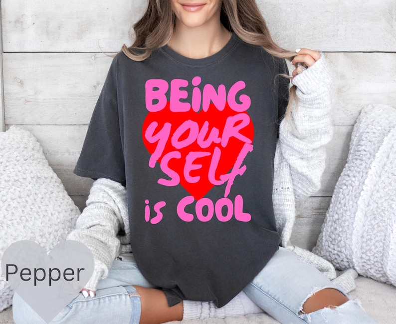 May include: A dark gray t-shirt with a pink and red heart graphic that says "Being Your Self is Cool".