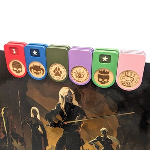 May include: Six rectangular plastic clips in red, blue, olive green, purple, light green, and pink, each featuring a circular wooden insert engraved with unique symbols including skulls, a paw print, an eye, a crown, and a musical note.