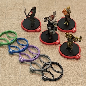 Puede incluir: Cinco figuras en miniatura sobre bases rojas y negras con números blancos. Las figuras son un guerrero con un hacha, un guerrero con un arco y flecha, un guerrero con un escudo, un guerrero con una espada y un guerrero con un bastón. También hay cinco anillos de plástico de colores con números blancos.