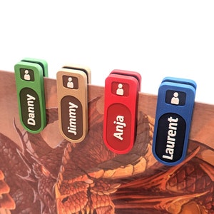 Puede incluir: Cuatro clips coloridos con nombres impresos en ellos. Los clips son verde, dorado, rojo y azul. Los nombres son Danny, Jimmy, Anja y Laurent.