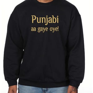 May include: Black sweatshirt featuring the gold text "Punjabi aa gaye oye!". The crew neck sweatshirt has long sleeves. The text is centrally positioned on the chest.