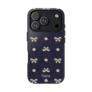 May include: A navy blue phone case with a pattern of white bows and small flowers. The name "Sara" is printed in white at the bottom. The case has a camera cutout for a smartphone.