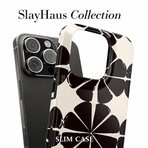 Puede incluir: Un tel&eacute;fono inteligente negro con una funda delgada con estampado floral crema y negro. La funda presenta un dise&ntilde;o abstracto repetitivo. El texto "SlayHaus Collection" y "SLIM CASE" son visibles.