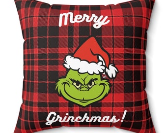 Puede incluir: Cojín cuadrado con un patrón de cuadros rojos y negros. El cojín presenta una cara verde del Grinch con un gorro de Papá Noel, con las palabras "Merry Grinchmas!" en escritura blanca.