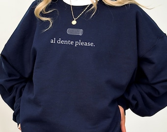 May include: A navy blue sweatshirt with a white graphic of a piece of pasta and the text "al dente please."