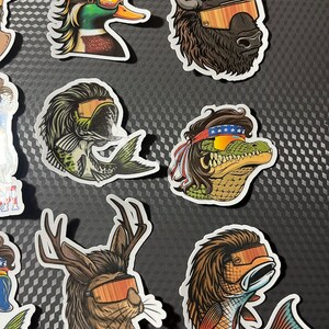 May include: A set of nine colorful stickers featuring various animals wearing sunglasses. The animals include a duck, a fish, a deer, a buffalo, a crocodile, and a fish. The stickers are all in a cartoon style and have a fun and whimsical feel.