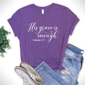 Puede incluir: Camiseta morada con texto blanco que dice "Su gracia es suficiente" y "2 Corintios 12:9".