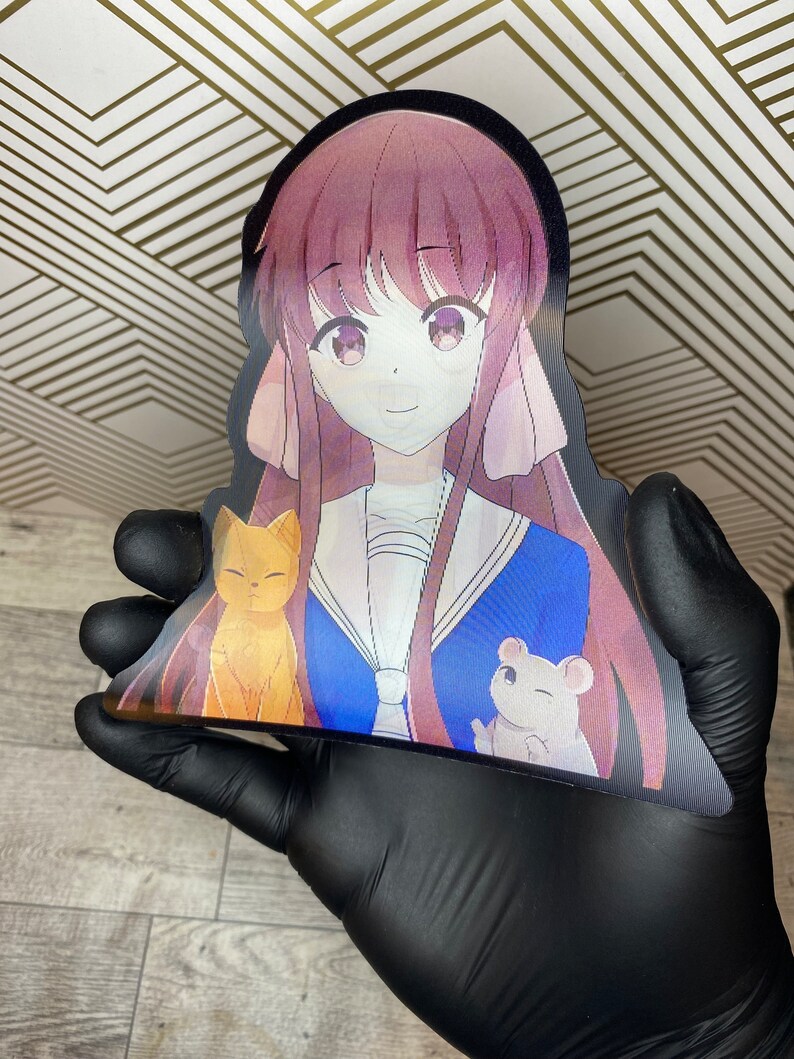 Puede incluir: Una pegatina con una chica de anime de dibujos animados con el pelo largo de color rosa que lleva un uniforme escolar azul y blanco. Est&aacute; sosteniendo un gato amarillo y un rat&oacute;n blanco.