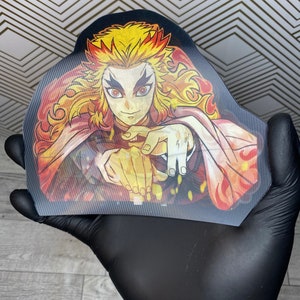 Pu&ograve; includere: Un adesivo con un personaggio con capelli arancioni fiammeggianti e occhi rossi, che indossa una veste rosso e bianca. Il personaggio &egrave; circondato da fiamme e ha un'espressione determinata.