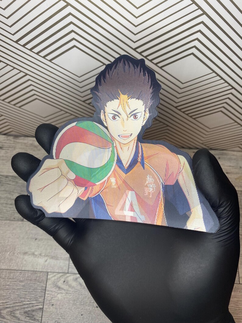 Puede incluir: Una pegatina con un personaje de anime con cabello casta&ntilde;o y ropa naranja y azul sosteniendo un bal&oacute;n de voleibol. El personaje sonr&iacute;e y tiene una expresi&oacute;n decidida. La pegatina est&aacute; impresa sobre un fondo blanco.