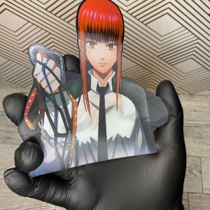 May include: A red-haired anime character with a white shirt and black tie, holding a chain with a silver charm. The character is depicted in a cartoon style.