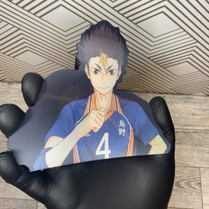 Puede incluir: Un personaje de anime con cabello negro y ojos marrones. El personaje lleva una camiseta azul y naranja con el n&uacute;mero 4 y el texto japon&eacute;s "烏野" en ella. El personaje est&aacute; levantando su mano derecha en un pu&ntilde;o.